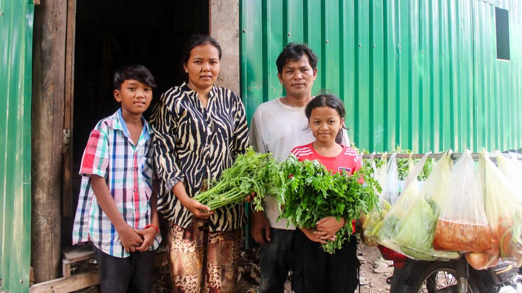 a family stands next to their motor bike filled with food to sell at the market
