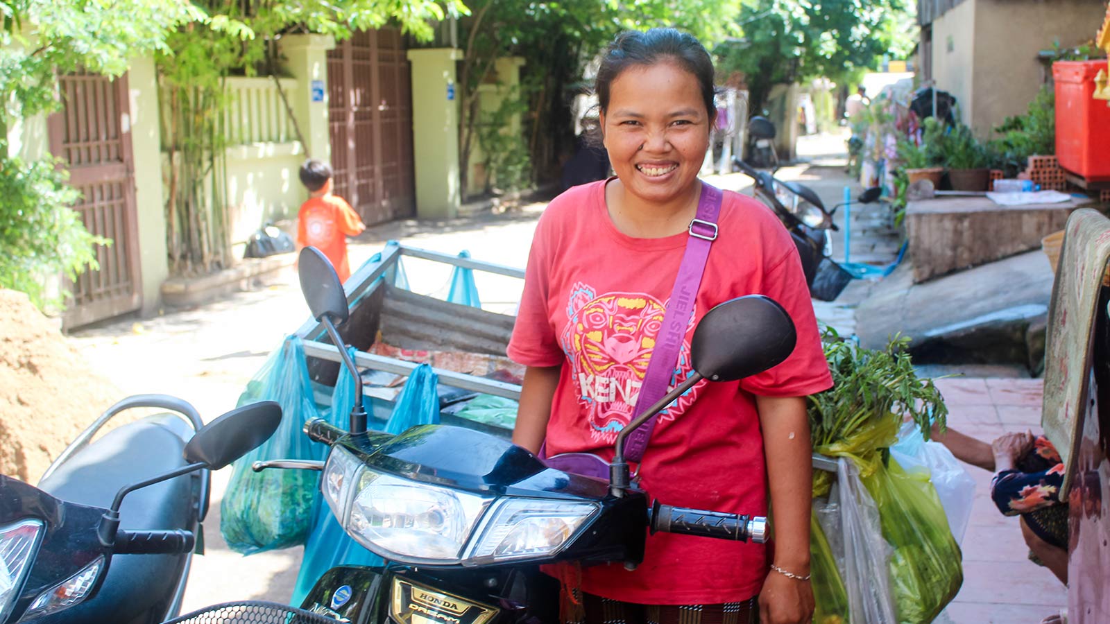 a mother stands next to her motor bike filled with food she can sell at the market