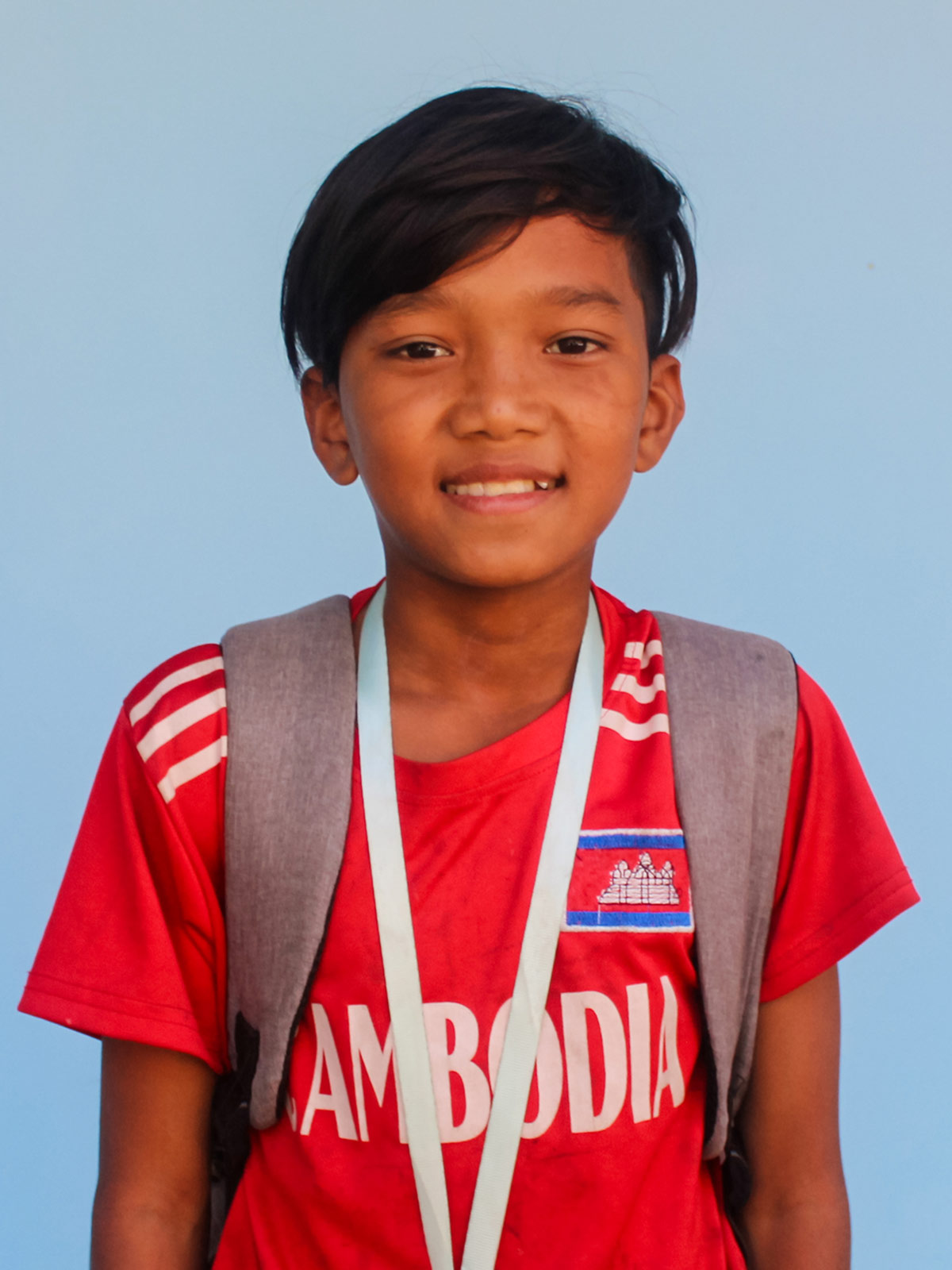 a sponsored boy in Cambodia wears a red soccer jersey and a backpack