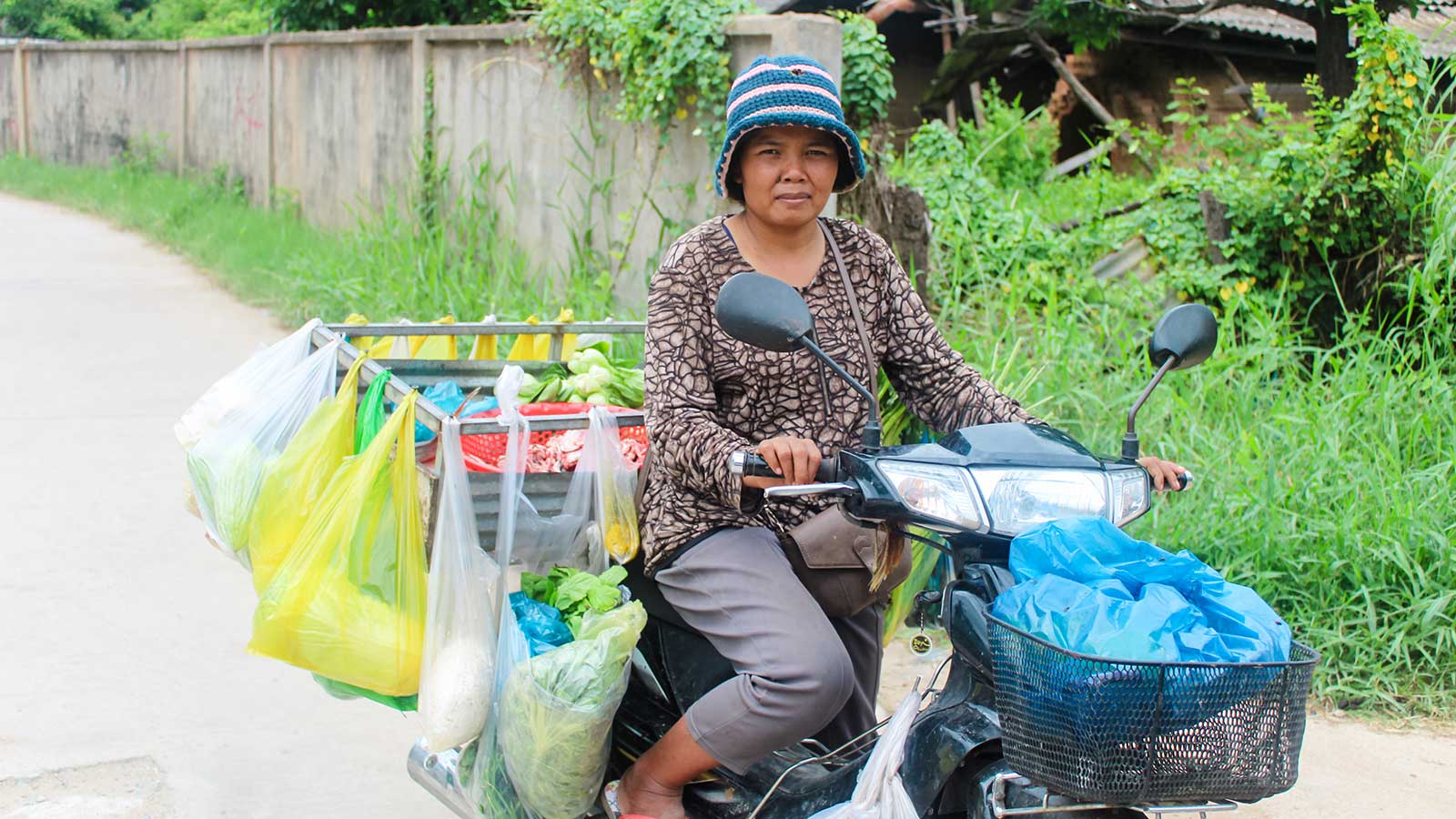 a mother sits on a motor bike filled with food she can sell at the market