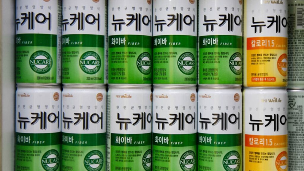 rows of tube feeding formula cans at a girl in a blue sweater receives nourishment through a feeding tube at Ilsan in Korea