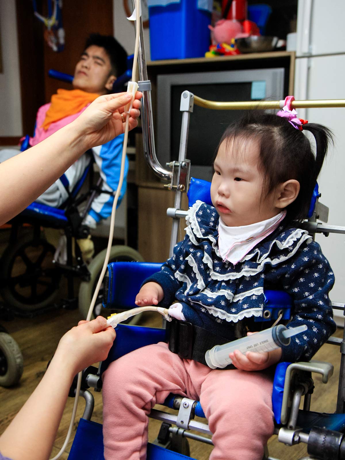 a girl in a blue sweater receives nourishment through a feeding tube at Ilsan in Korea