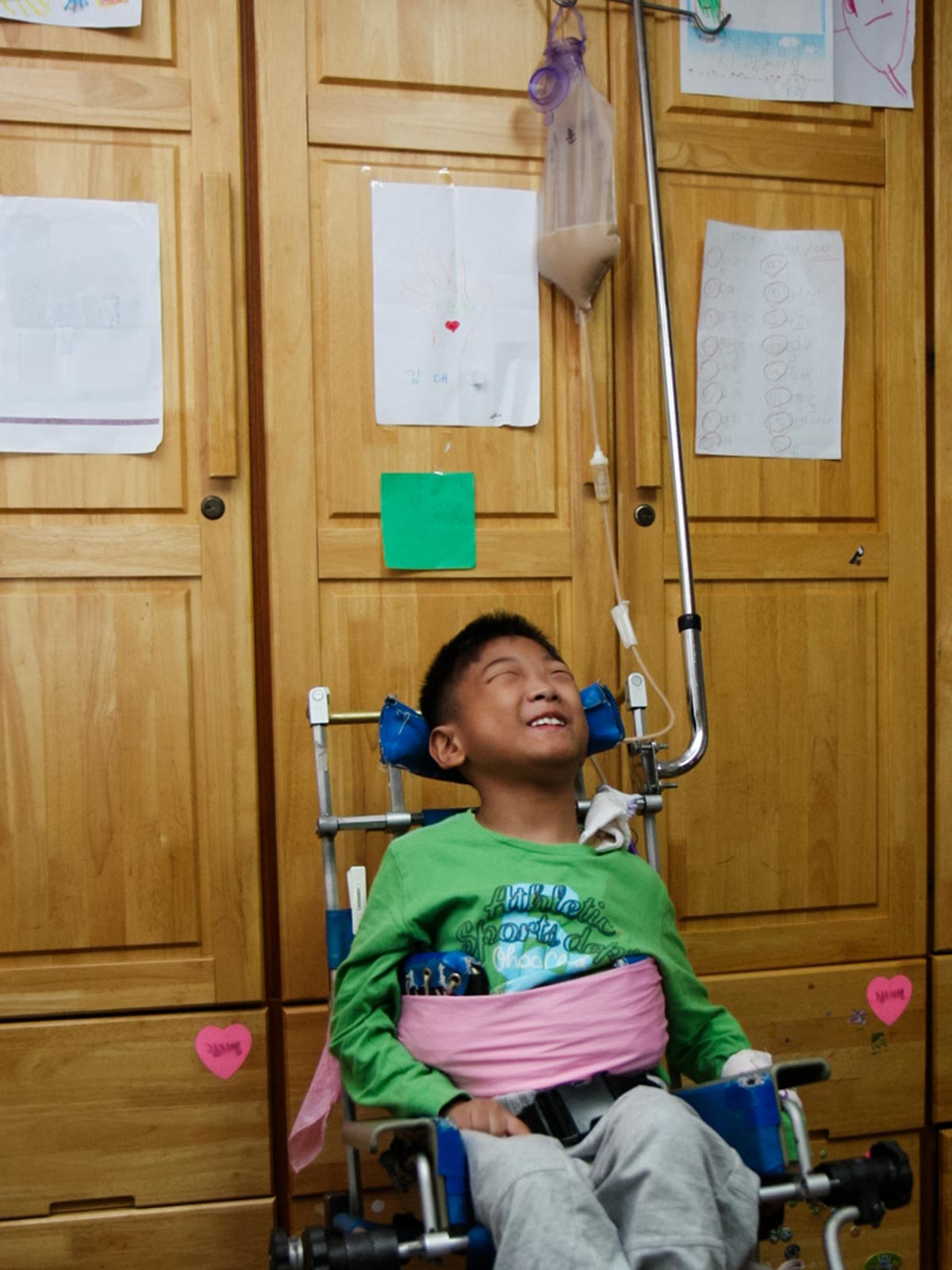 a boy in a green shirt smiles as he receives nourishment through a feeding tube at Ilsan in Korea