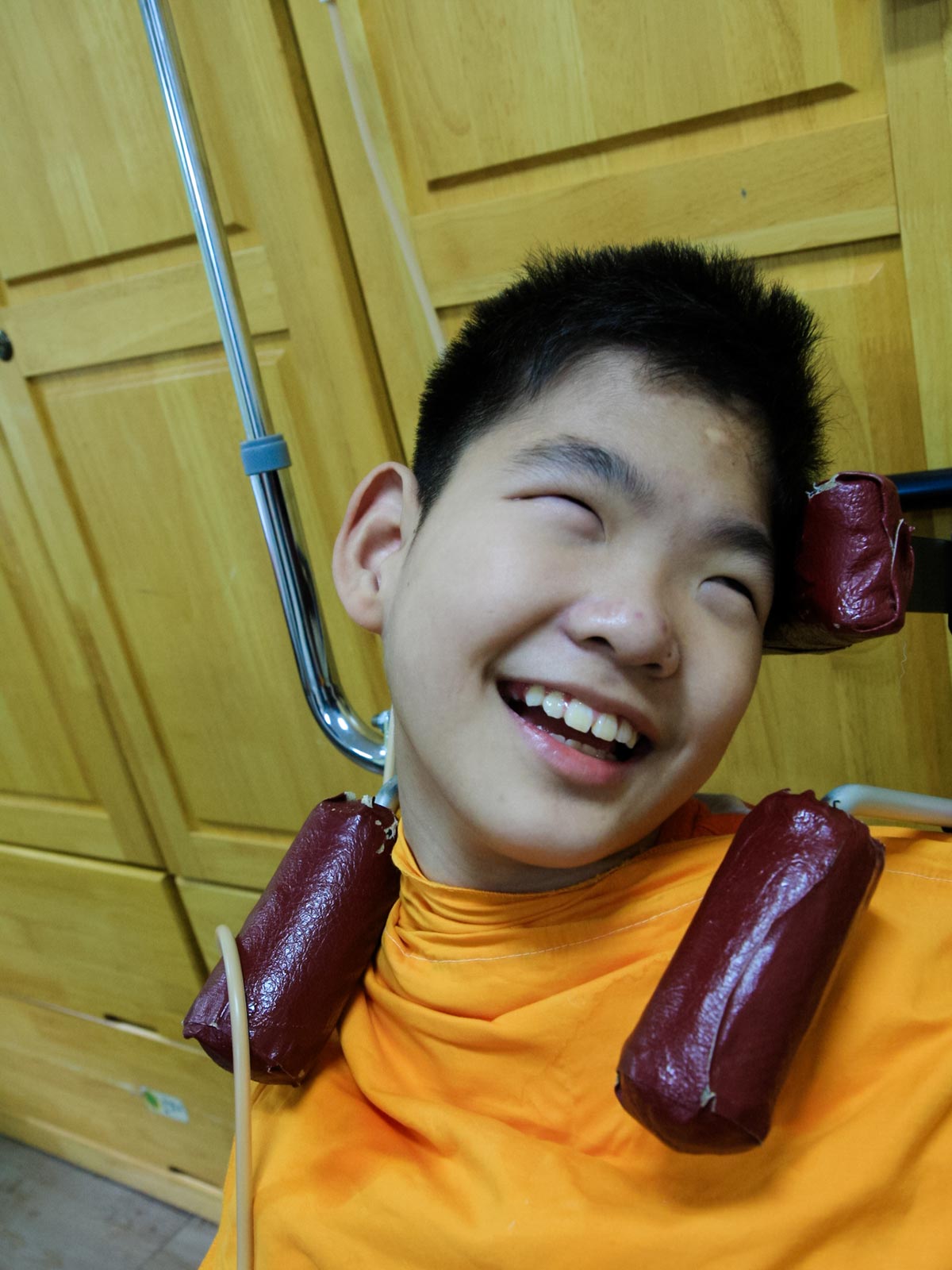 a boy in an orange shirt smiles as he receives nutrition through a feeding tube at Ilsan in Korea