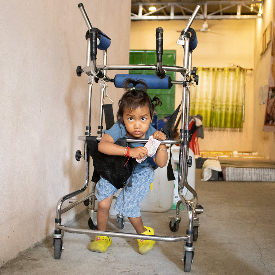 Sophea, a child in special needs foster care in Cambodia, using a walker to help her learn to walk independently.