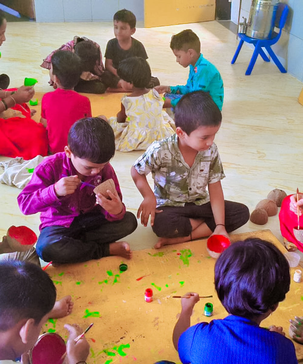 children sit in a circle on the floor and paint for summer camp in India