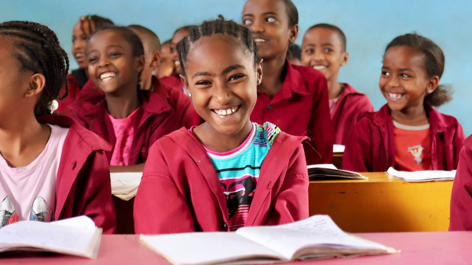 Little girl smiling in a classroom looking at the camera.