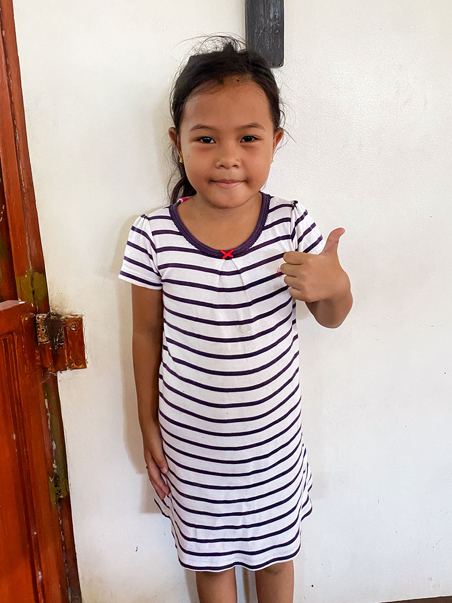 a girl in a striped dress smiles and gives a thumbs up at a feeding center in the Philippines