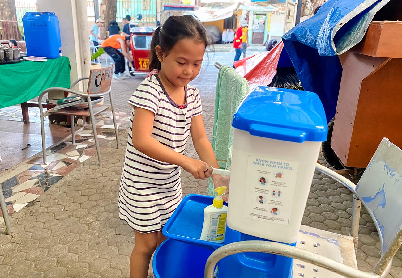 a girl in a striped dress uses a handwashing station at the feeding center in the Philippines