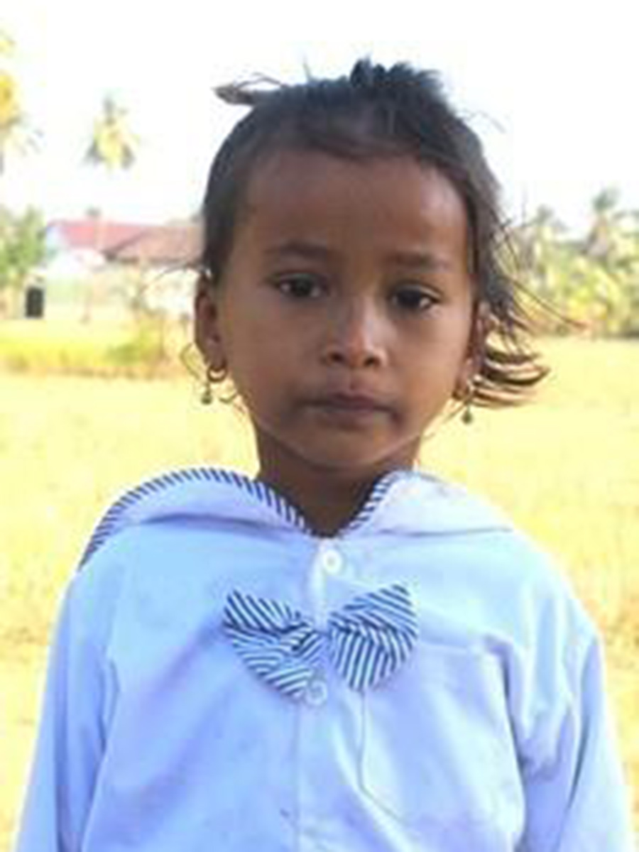 a sponsored girl in a white uniform stands in a field in Cambodia