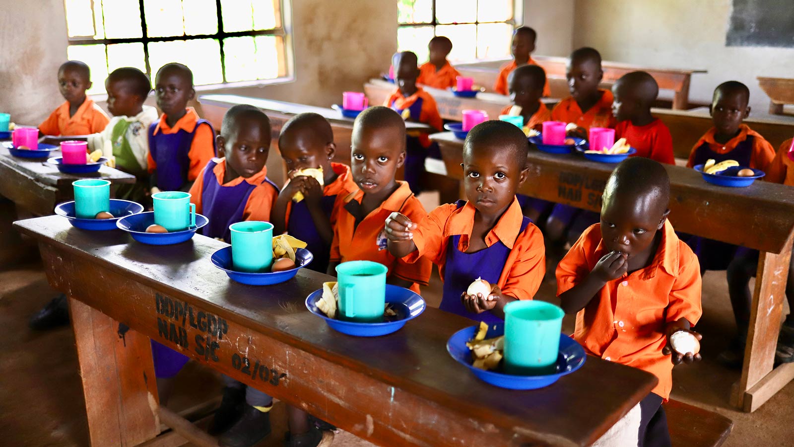 children smile and eat their school lunches at preschool in Uganda