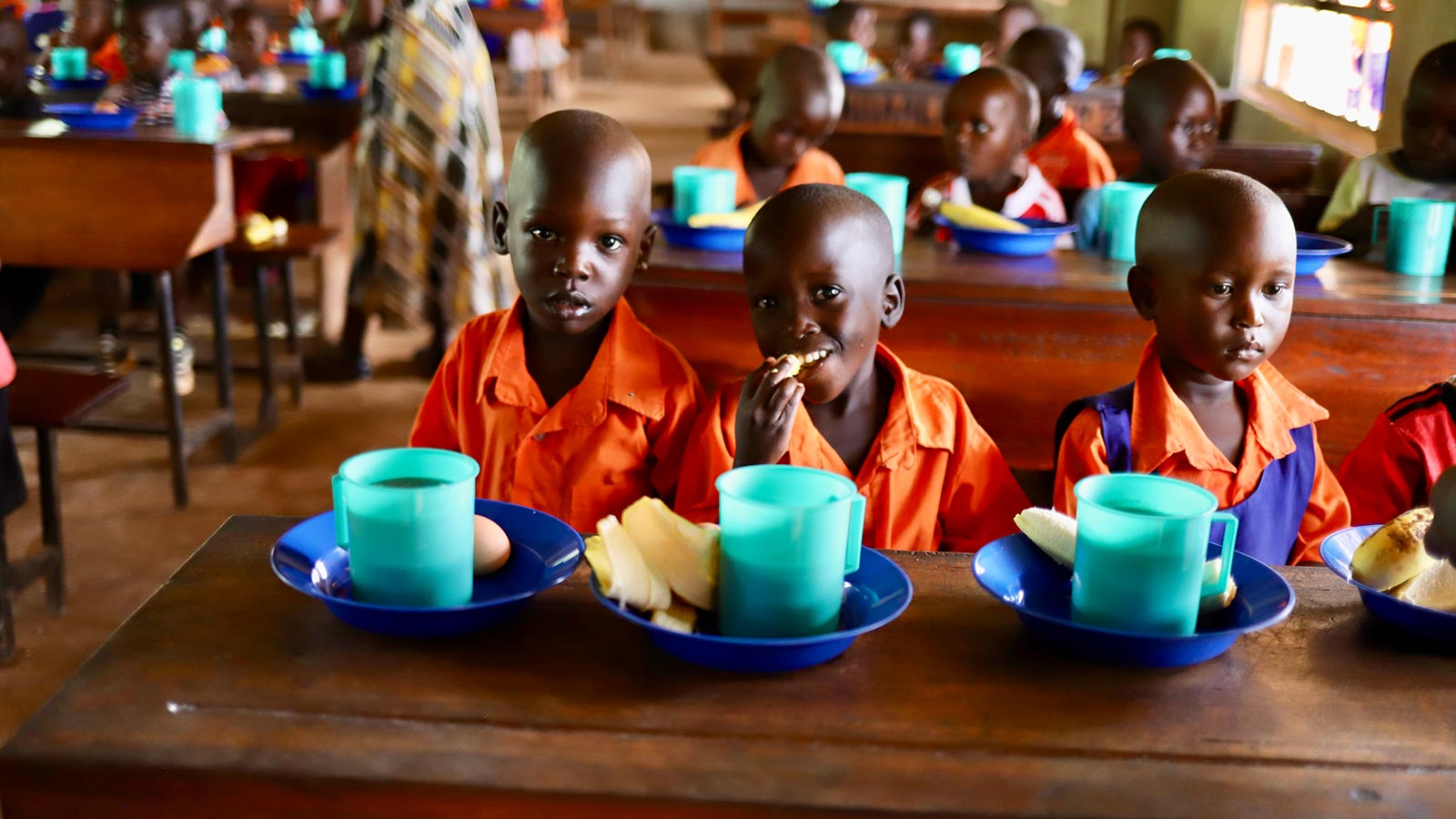children smile and eat their school lunches at preschool in Uganda