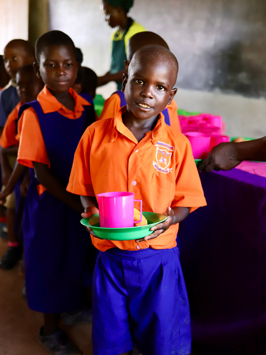 a boy in a school uniform holds a plate of school lunch in Uganda