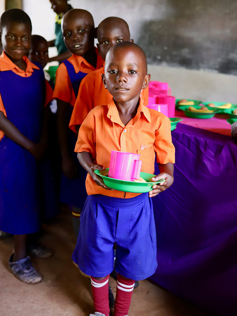 a boy in a school uniform holds a plate of school lunch in Uganda