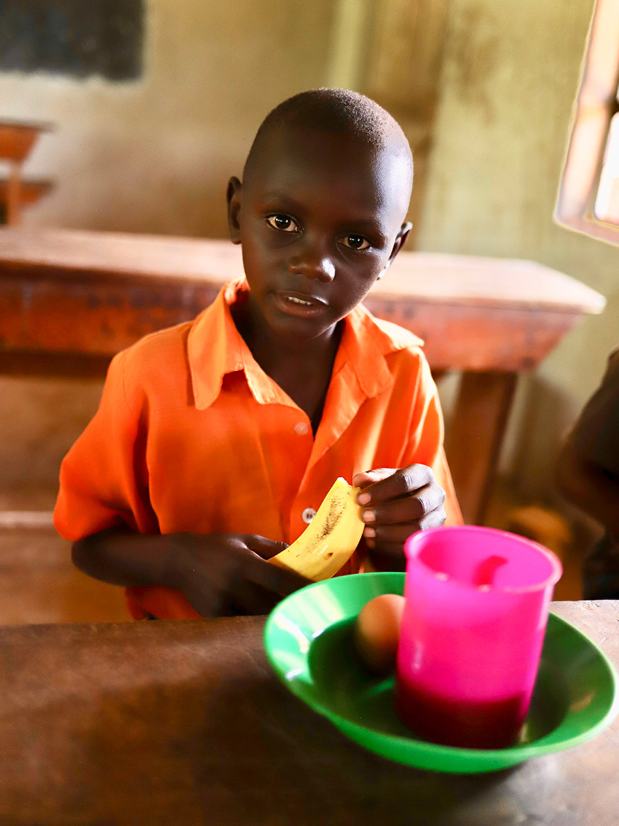 a boy in a school uniform eats his school lunch in Uganda