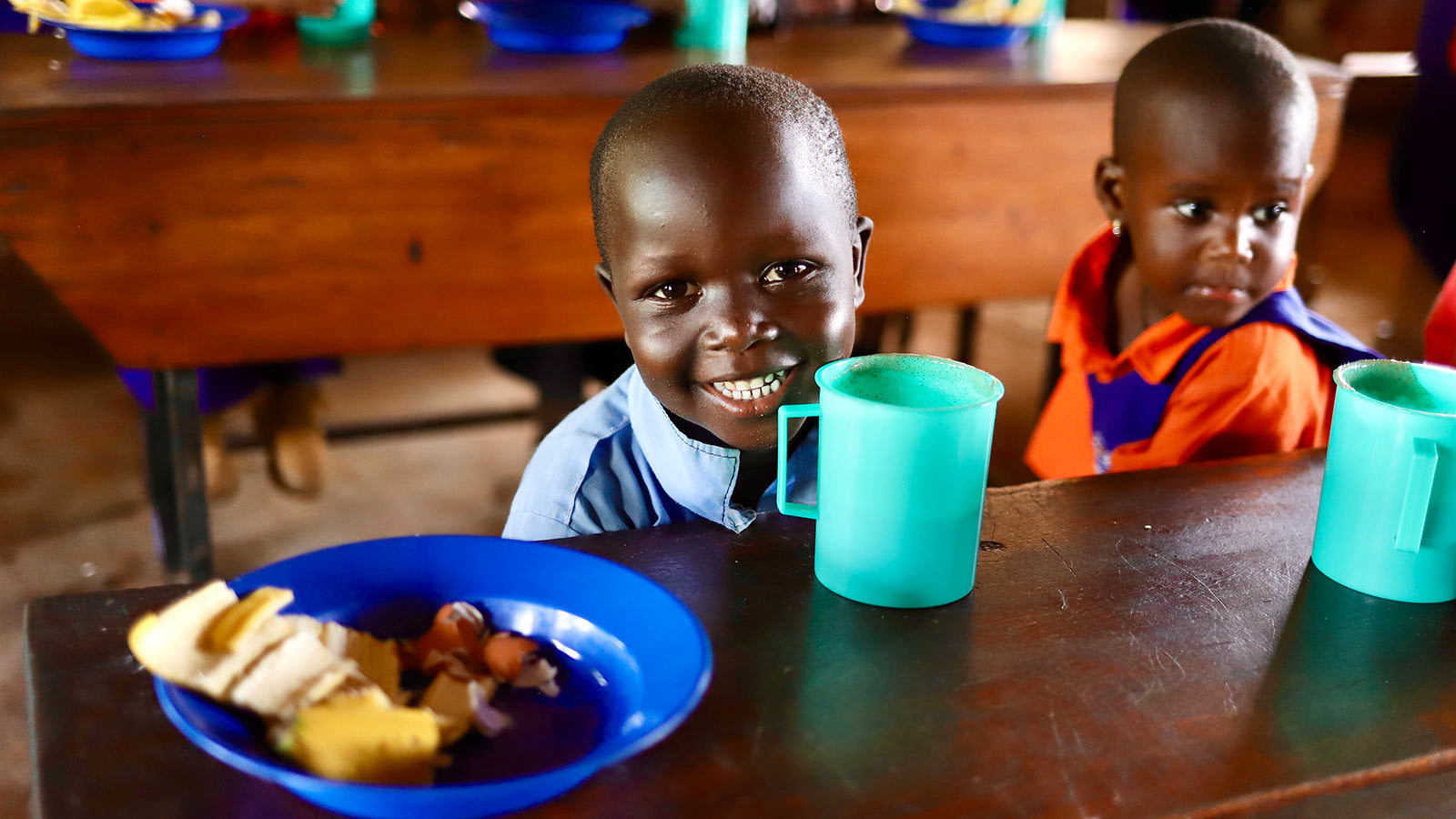 a boy in a school uniform smiles with his school lunch in Uganda