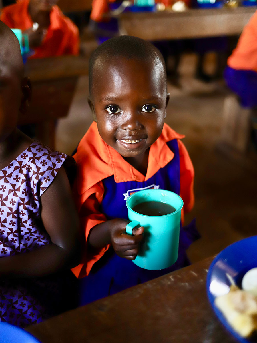 a girl in a school uniform smiles with her school lunch in Uganda