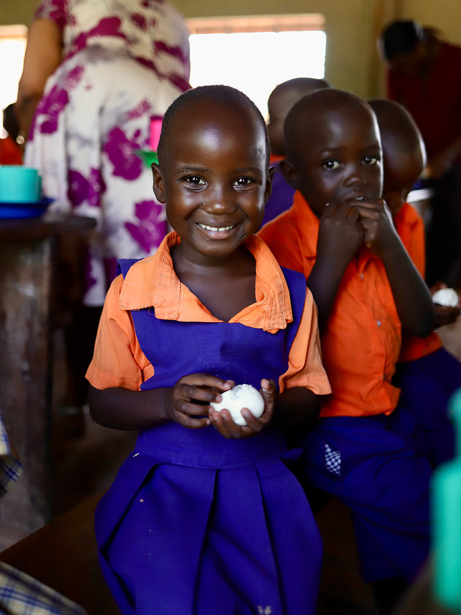 a girl in a school uniform smiles with her school lunch in Uganda