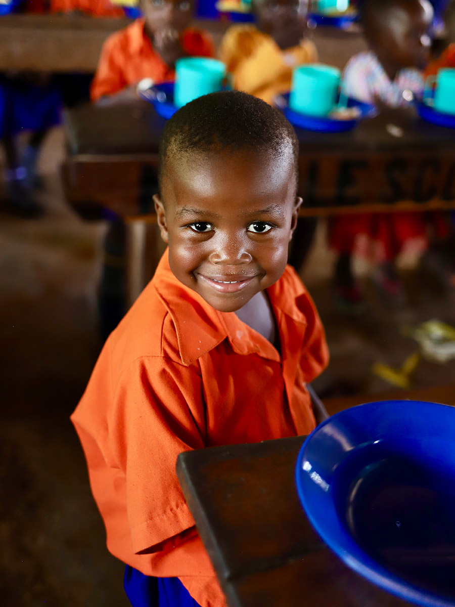 a boy in a school uniform smiles with his school lunch in Uganda