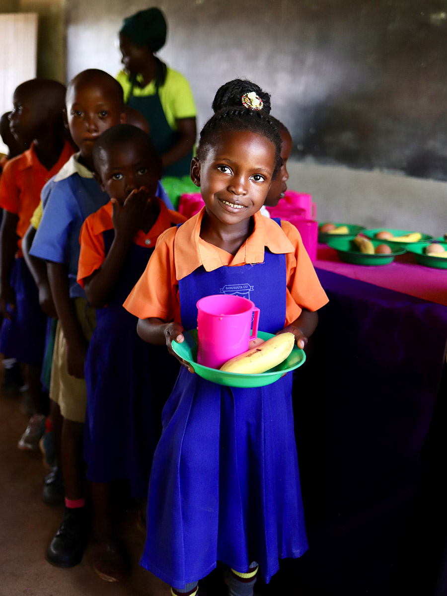a girl in a school uniform holds a plate of school lunch in Uganda