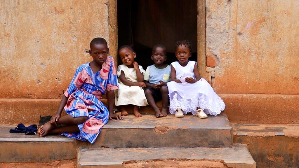three little girls and a boy sit on the doorstep of their home in rural Uganda