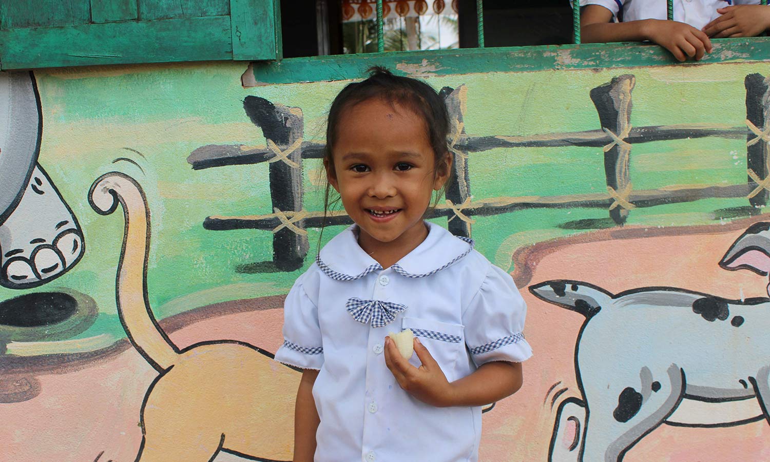 a little girl in a white school uniform smiles with her school lunch in Cambodia