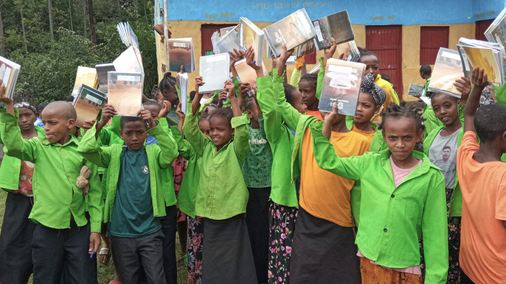 Group of children holding up school supplies outside their school